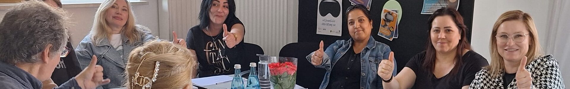 Lerner*innen sitzen an einem großen Tisch, lächeln und zeigen "Daumen hoch" in die Kamera.