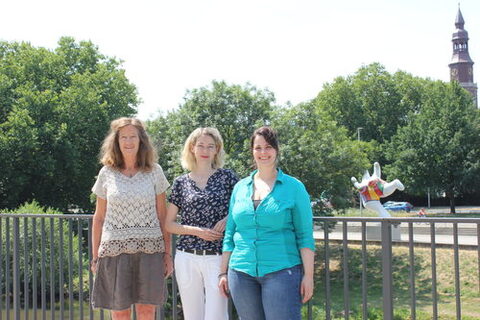 Gruppenbild von drei Frauen draußen in Park, im Hintergrund ein Kirchturm