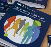 Liegender Aktenordner mit der Beschriftung „Alpha-Kurzdiagnostik – DVV-Rahmencurriculum Schreiben und Lesen“