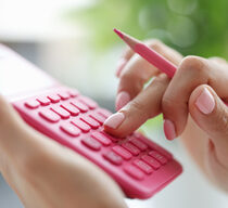 Rechnen lernen mit dem Taschenrechner: Nahaufnahme einer Hand, die an einem pinkfarbenen Taschenrechner tippt und einen gleichfarbigen Stift hält.