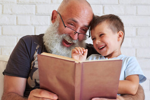 Älterer Mann und ein Kind schauen gemeinsam in ein Buch. Beide lächeln.