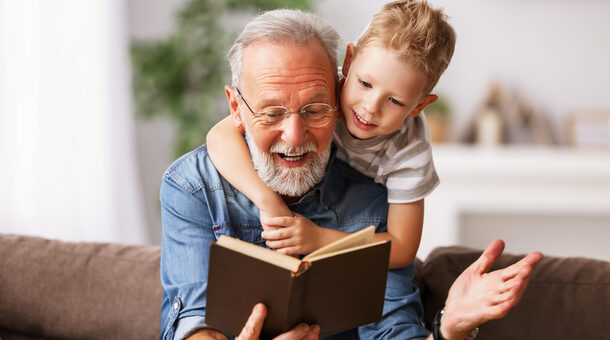 Alterer Mann hält ein Buch in der Hand, ein Junge umarmt ihn
