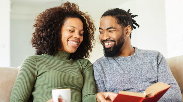 Eine Frau und ein Mann sitzen auf einer Couch und schauen gemeinsam in ein geöffnetes Buch.
