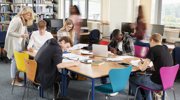 Busy College Library With Teacher Helping Students At Table