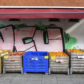 Unterschiedliches Obst in großen Boxen vor einer Wand, die mit Graffiti besprüht ist.