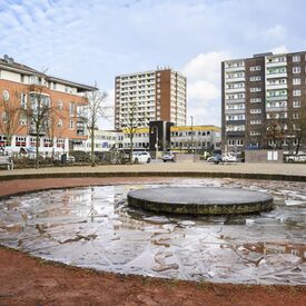 Ein Platz mit einem Brunnen im Vordergrund und Hochhäusern im Hintergrund.
