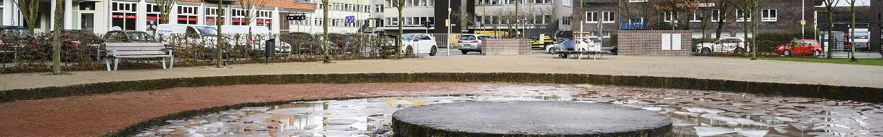 Ein Platz mit einem Brunnen im Vordergrund und Hochhäusern im Hintergrund.