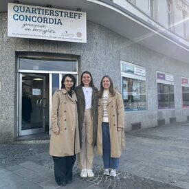 Drei Frauen stehen vor einem Haus und lächeln in die Kamera.