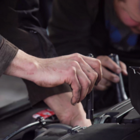 Nahaufnahme von Händen, die in einer Werkstatt etwas an einem Auto reparieren.